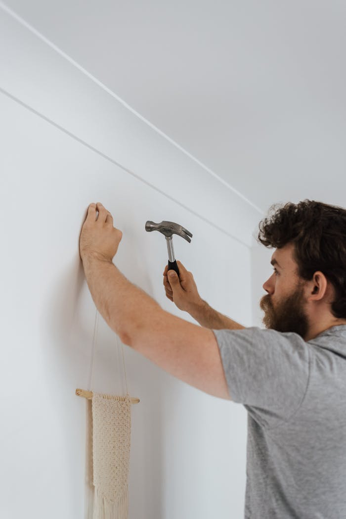 Man using a hammer to hang a decoration on a wall indoors.