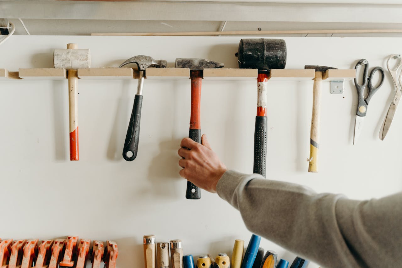 Close-up of a hand reaching for a hammer in a workshop with various tools.